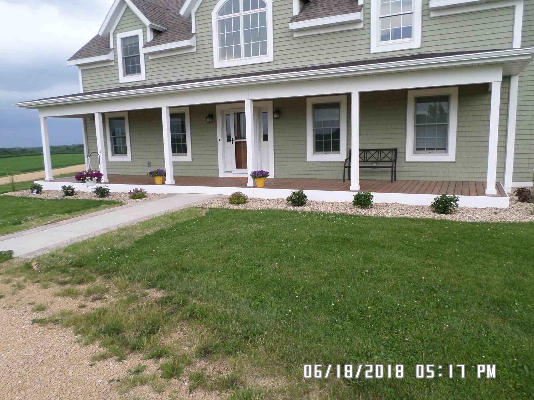 Front yard landscaping with foundation plantings, wraparound porch, and gravel drive, Platteville WI