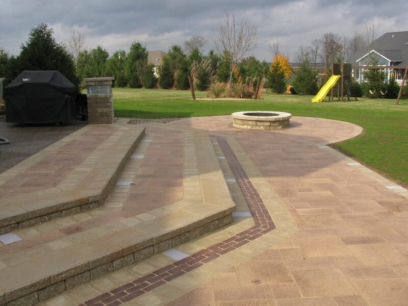 Covered porch with paver patio, seating wall, and fire pit beside a home