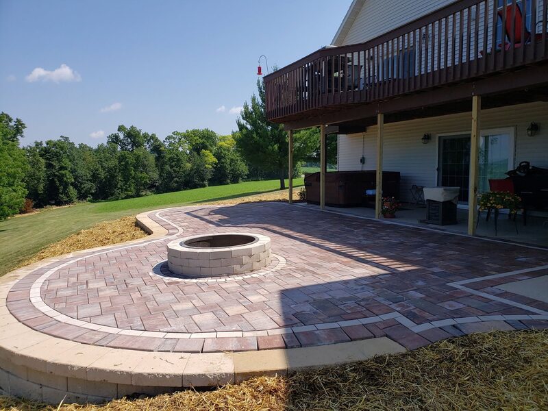 Brick paver patio with circular fire pit and wood deck overlooking a lawn